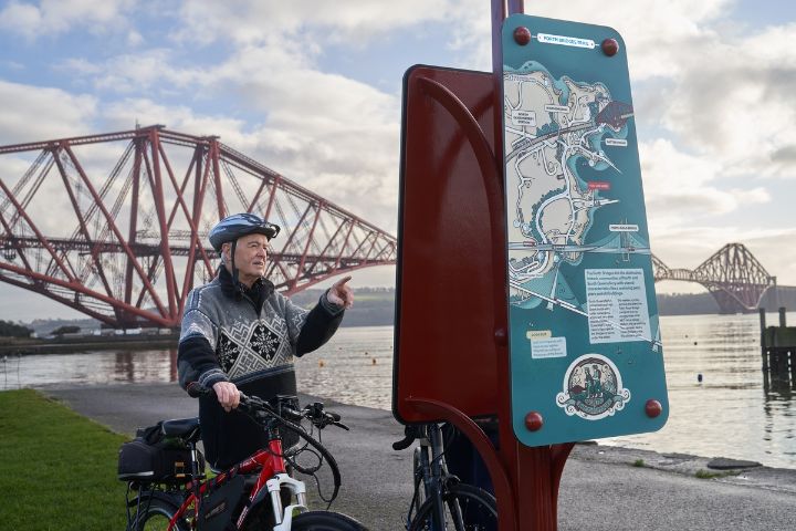 An old man with a bike inspects a map of North Queensferry
