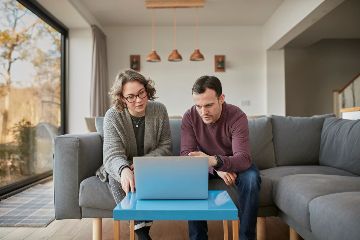 Two people on a sofa behind their laptop.
