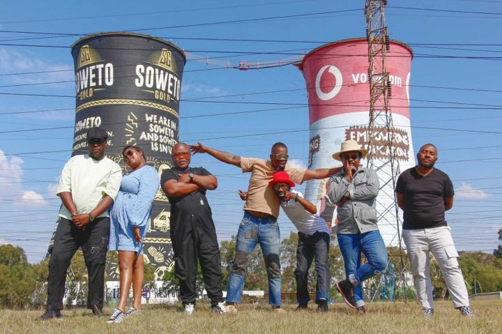 Promotional shot of a band standing in front of two industrial chimneys