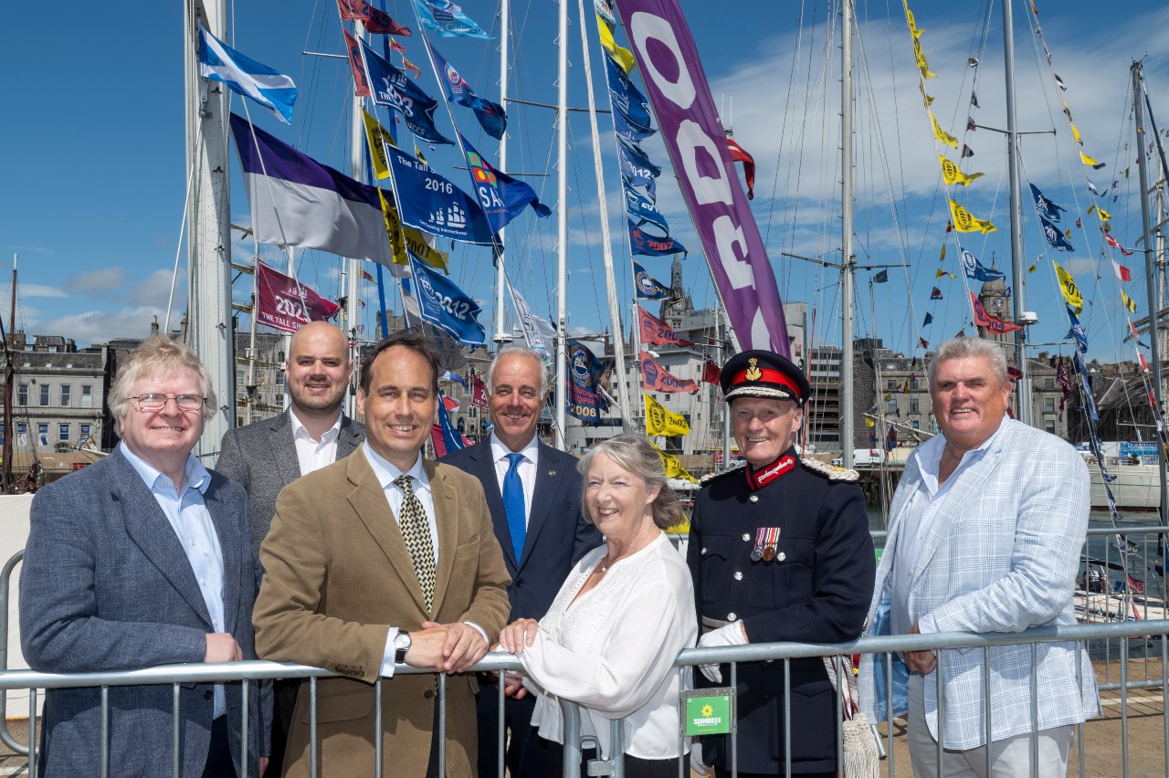 People posing in front of ships in a harbour