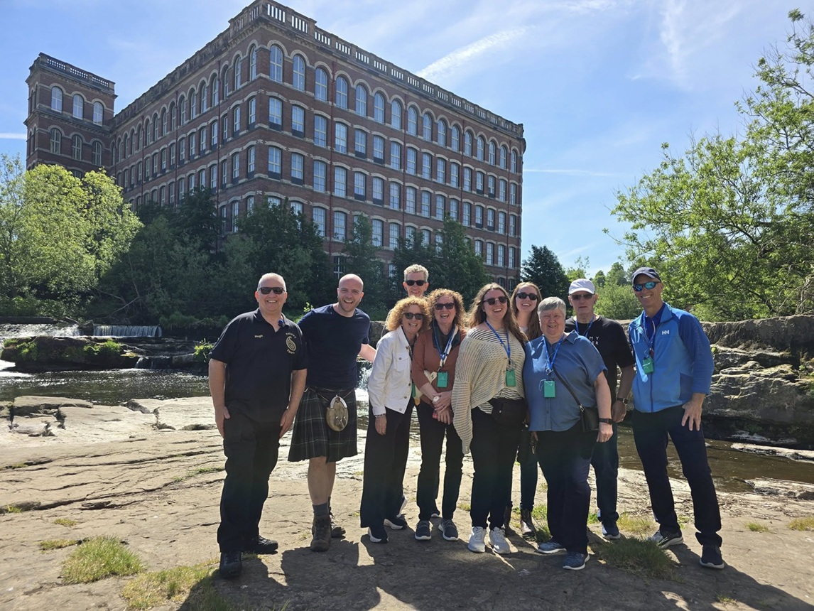 A group of people standing together smiling to a camera outside on a sunny day