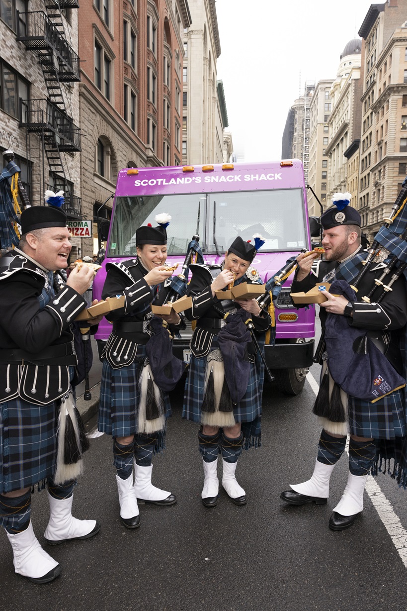 A group of pipers standing in front of a vehiclein a busy New York City street