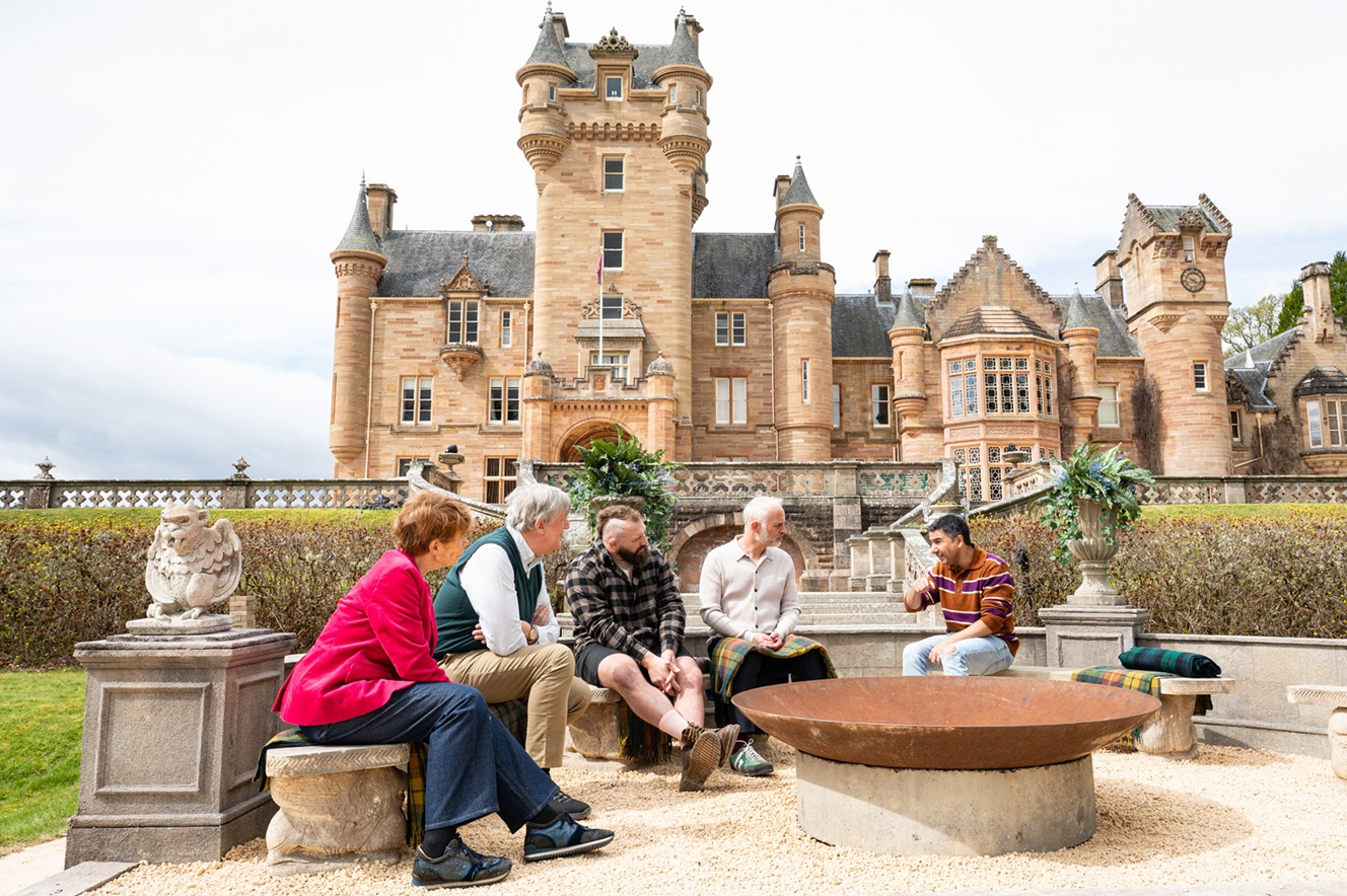 A group of people sitting around a fire pit in front of a castle