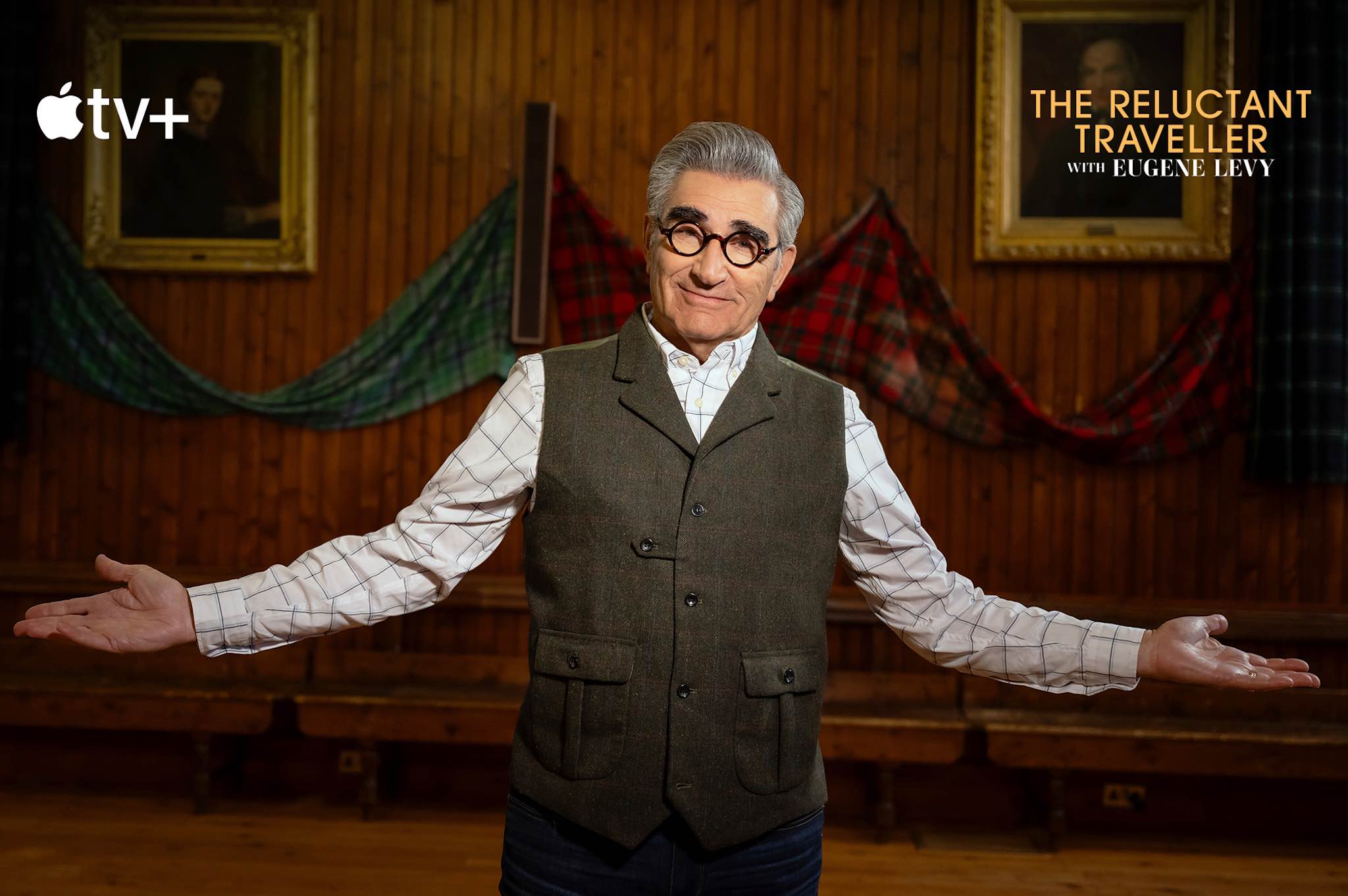 A person standing in a room with tartan banners in the background, with their arms open