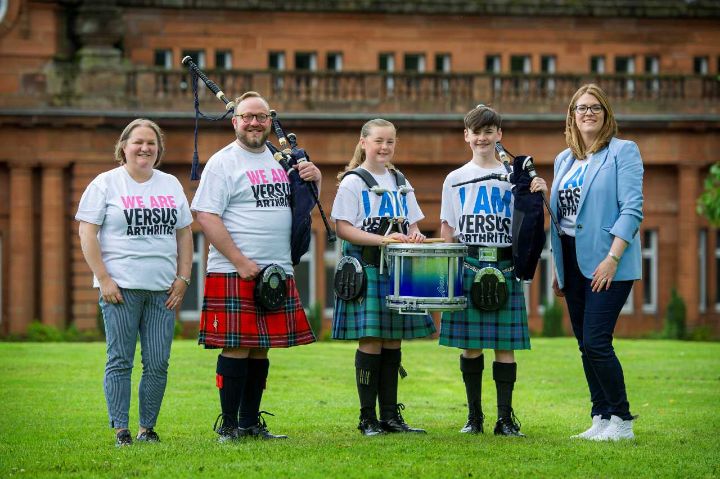 A group of  people with pipes and drums posing in front of a historical building