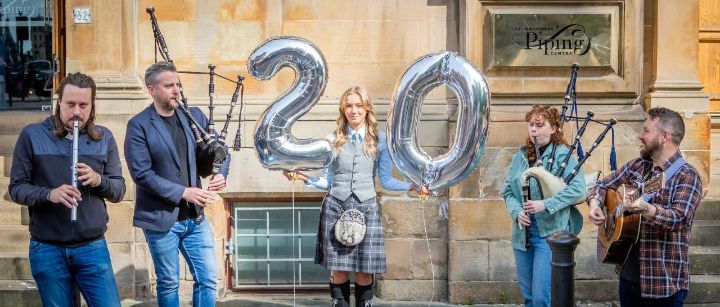 Musicians posing with instruments and a number 20 balloon outside an historic building