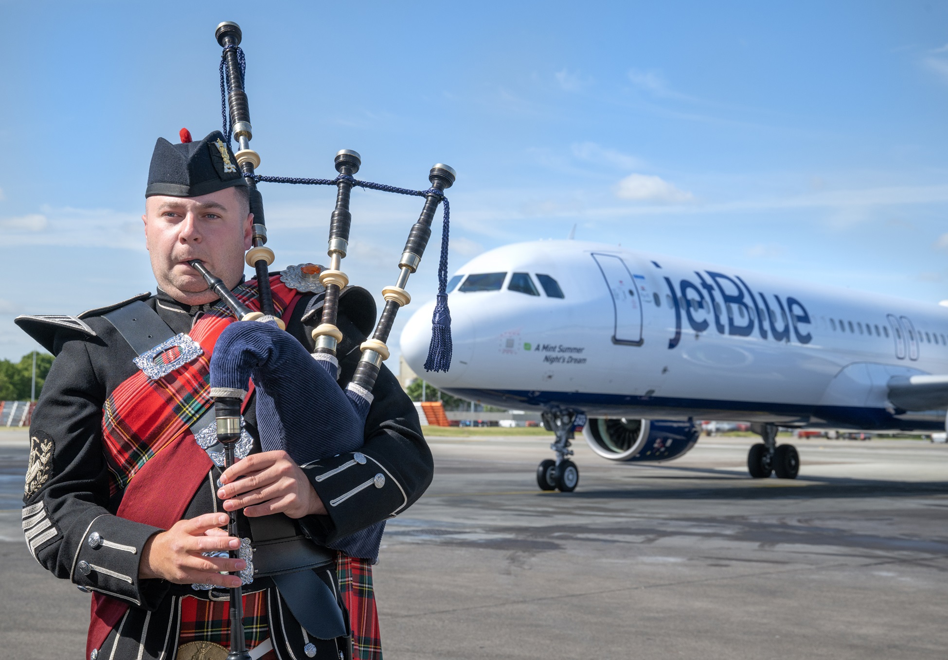 A bagpiper with a JetBlue airplane behind him.