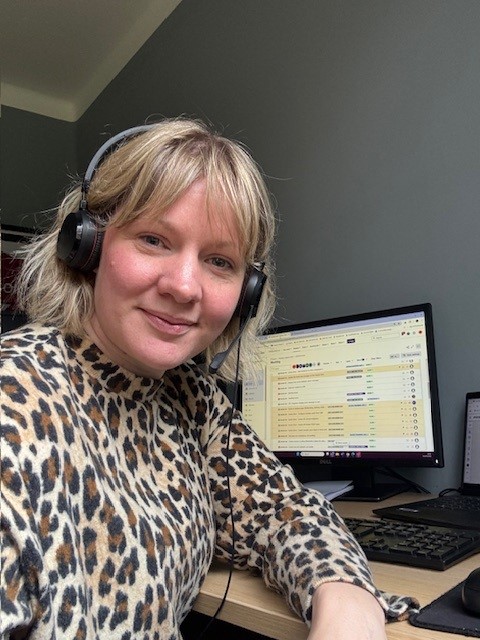 Sam taking a selfie while working, with her headset on and her screen behind her