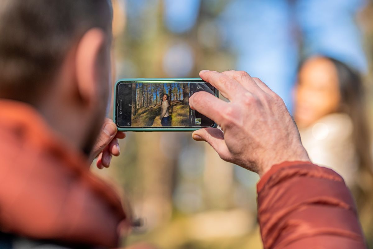 A person taking a picture of a woman amongst trees.