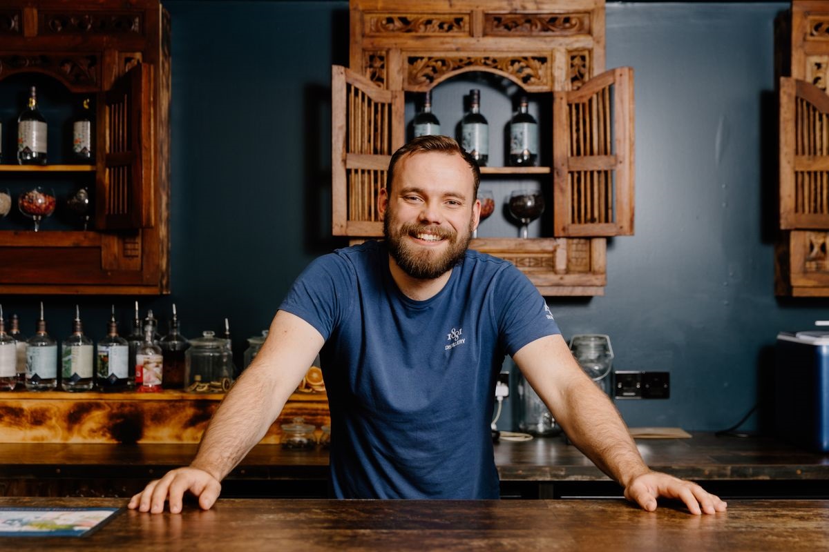 A distillery working greeting people from behind the bar.