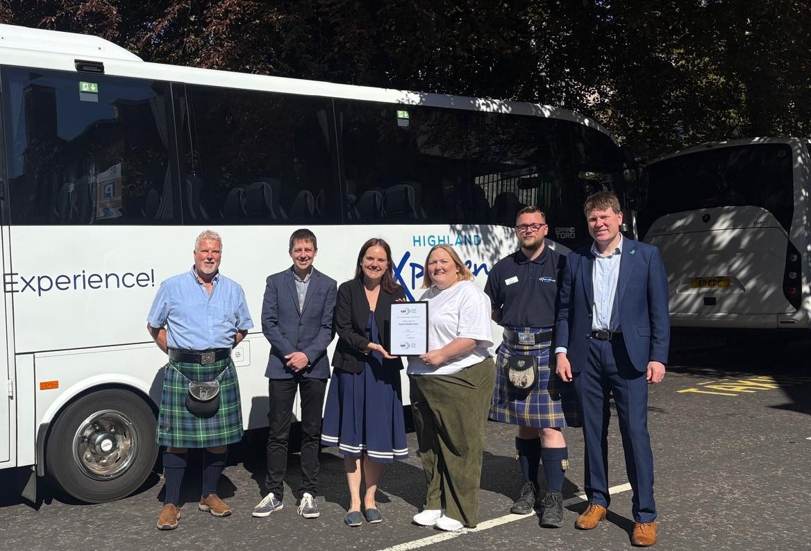 A group of people stand infront of the side of a coach holding a certificate