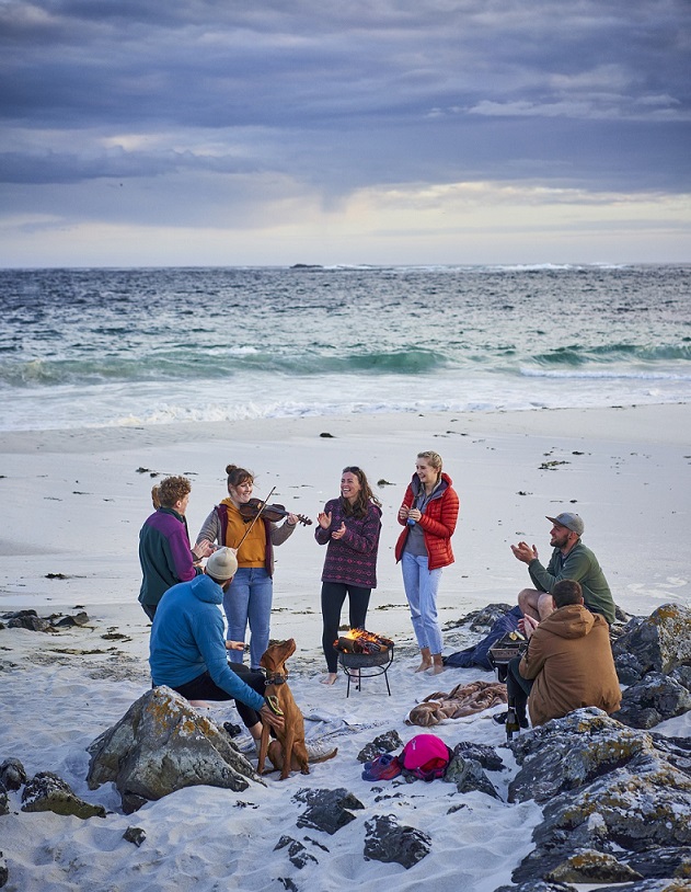A group of people standing together in a beach one person is holding a musical instrument