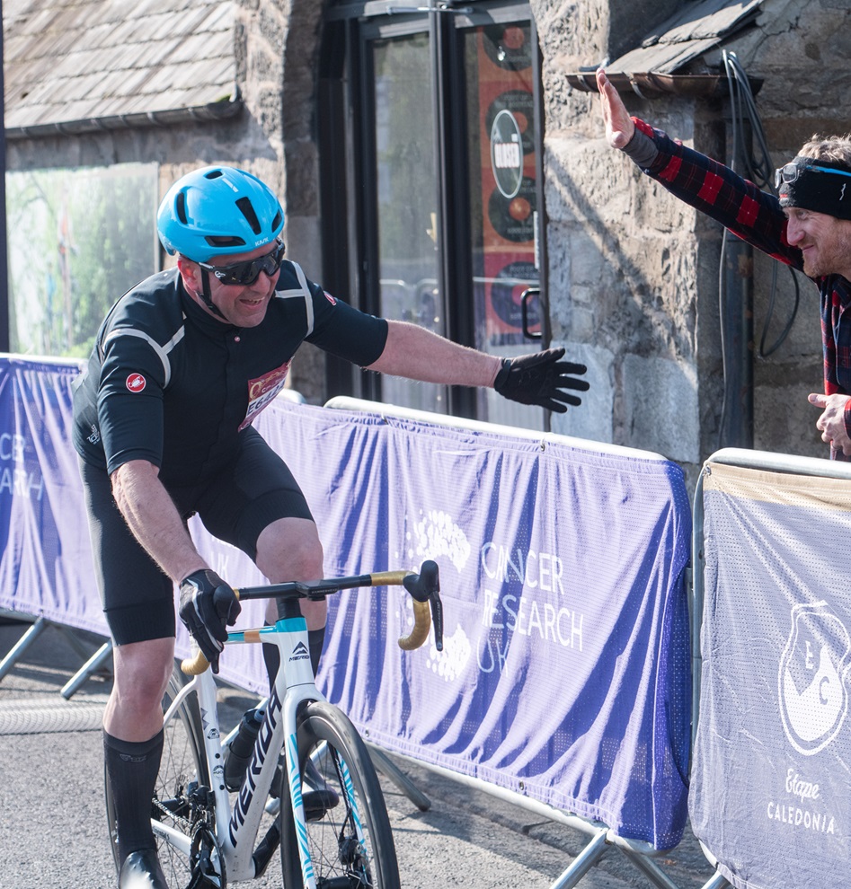A cyclist in a road race being encourage by a by stander