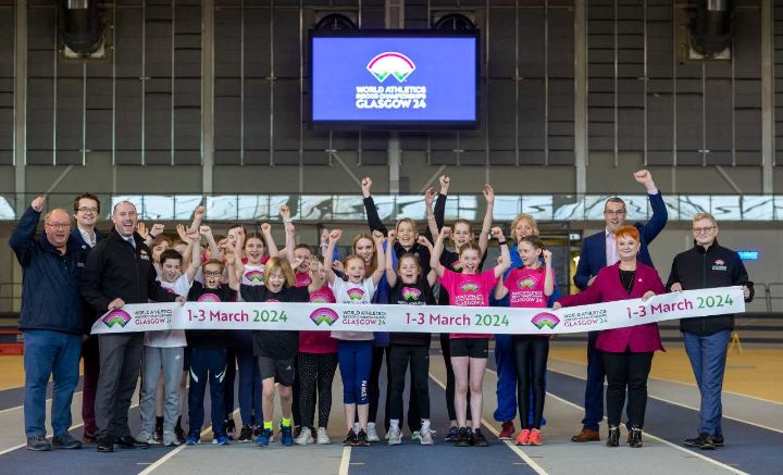 People cheering in front of a branded finishing tape in an athletics arena