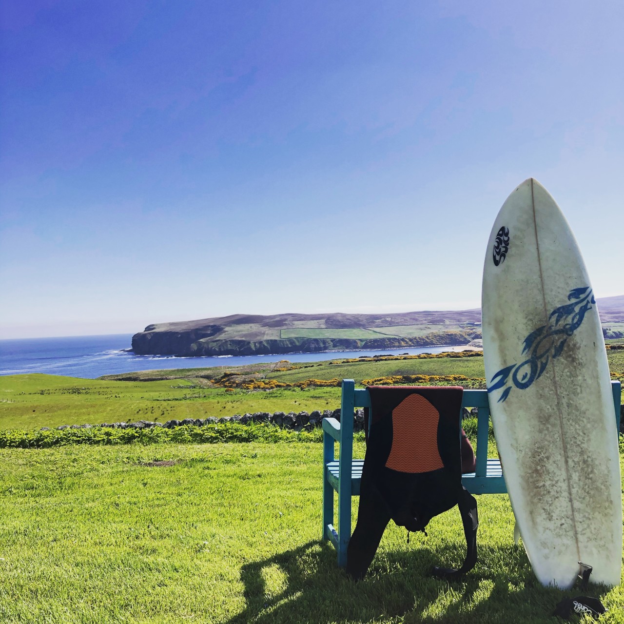 Surfboard leaning against a garden seat with coastal views in background