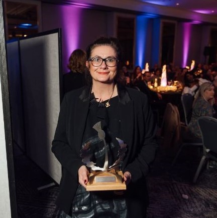 A person standing in a dark large room holding a awards trophy