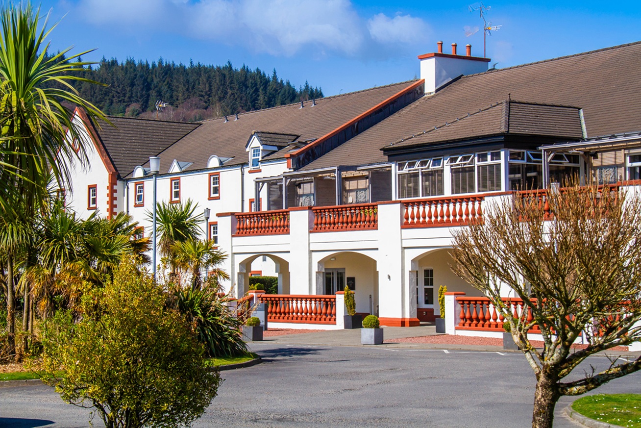 Image of exterior Auchrannie Resort behind a lavish garden with hedges lining a small pond and water feature.