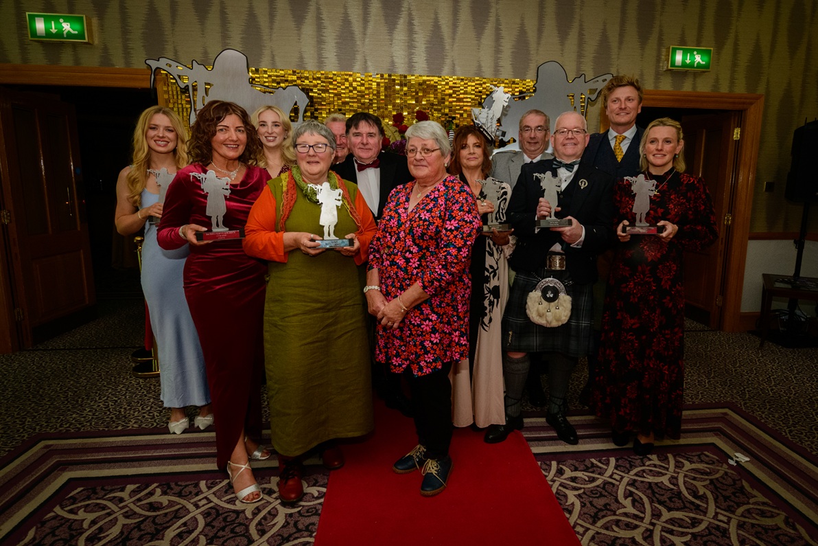A group of people gathered together in a room holding awards