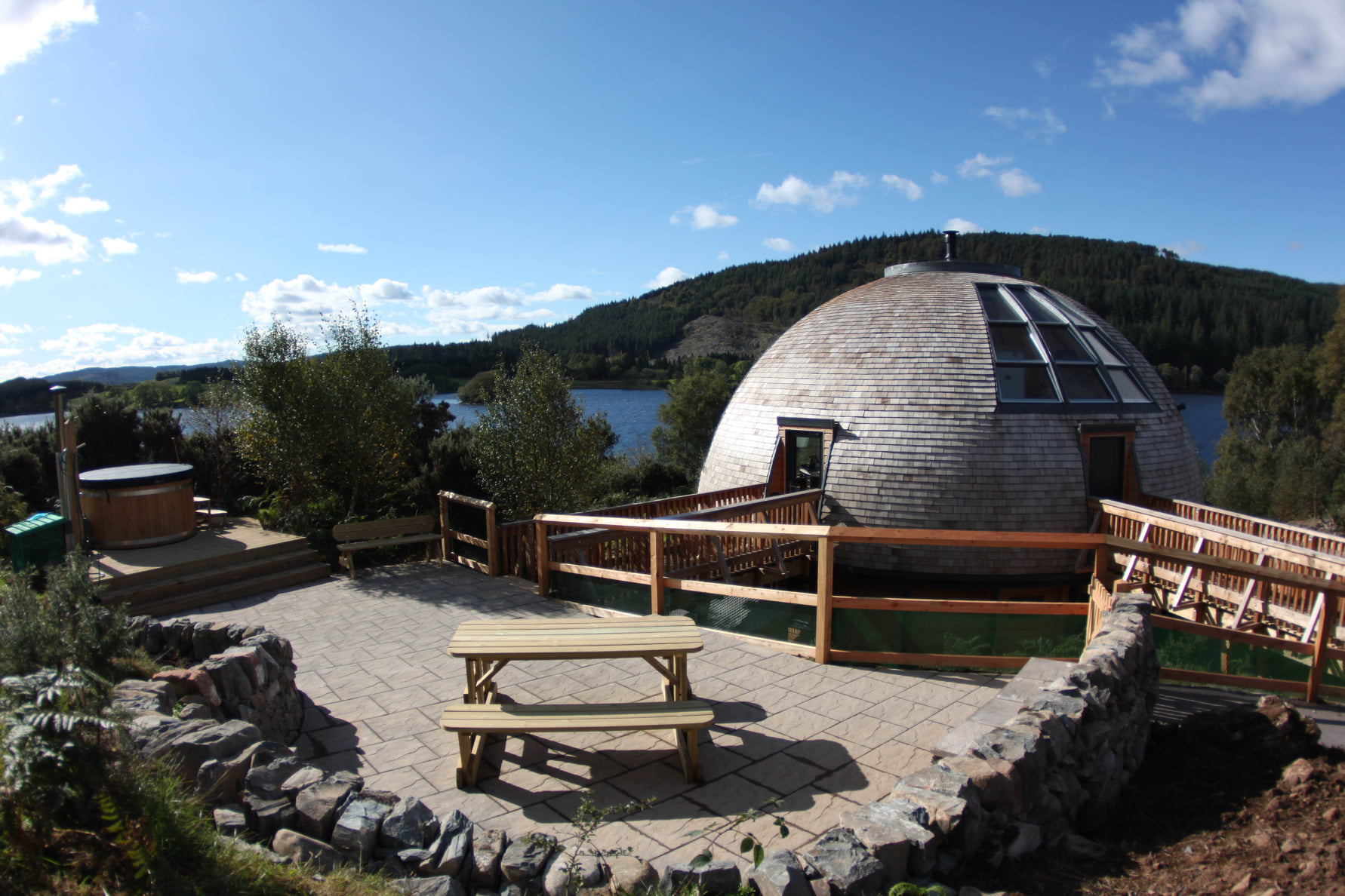 The exterior of Loch Ken Eco Bothies, globe-shaped self-catering lodges with a hot tub and picnic bench beside it.