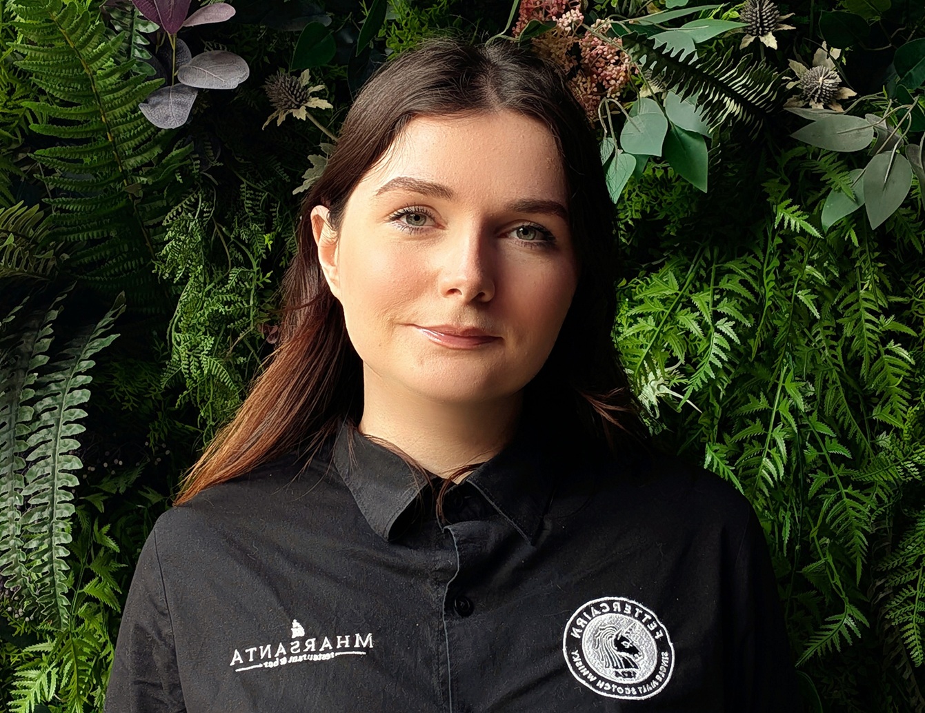 An image of a girl smiling in front of a green shrubbery backdrop