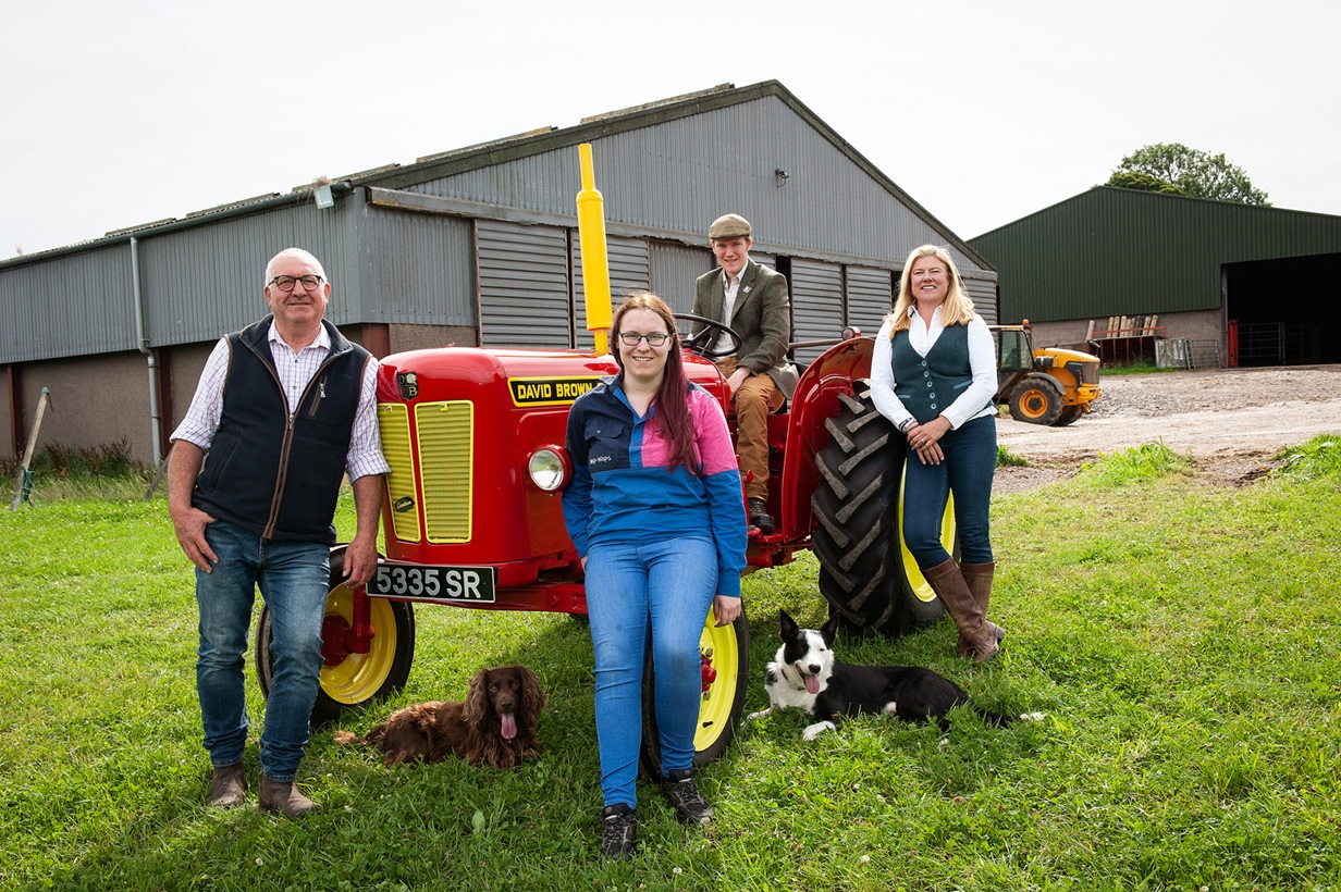 4 people smiling, standing next to a tractor in a field.