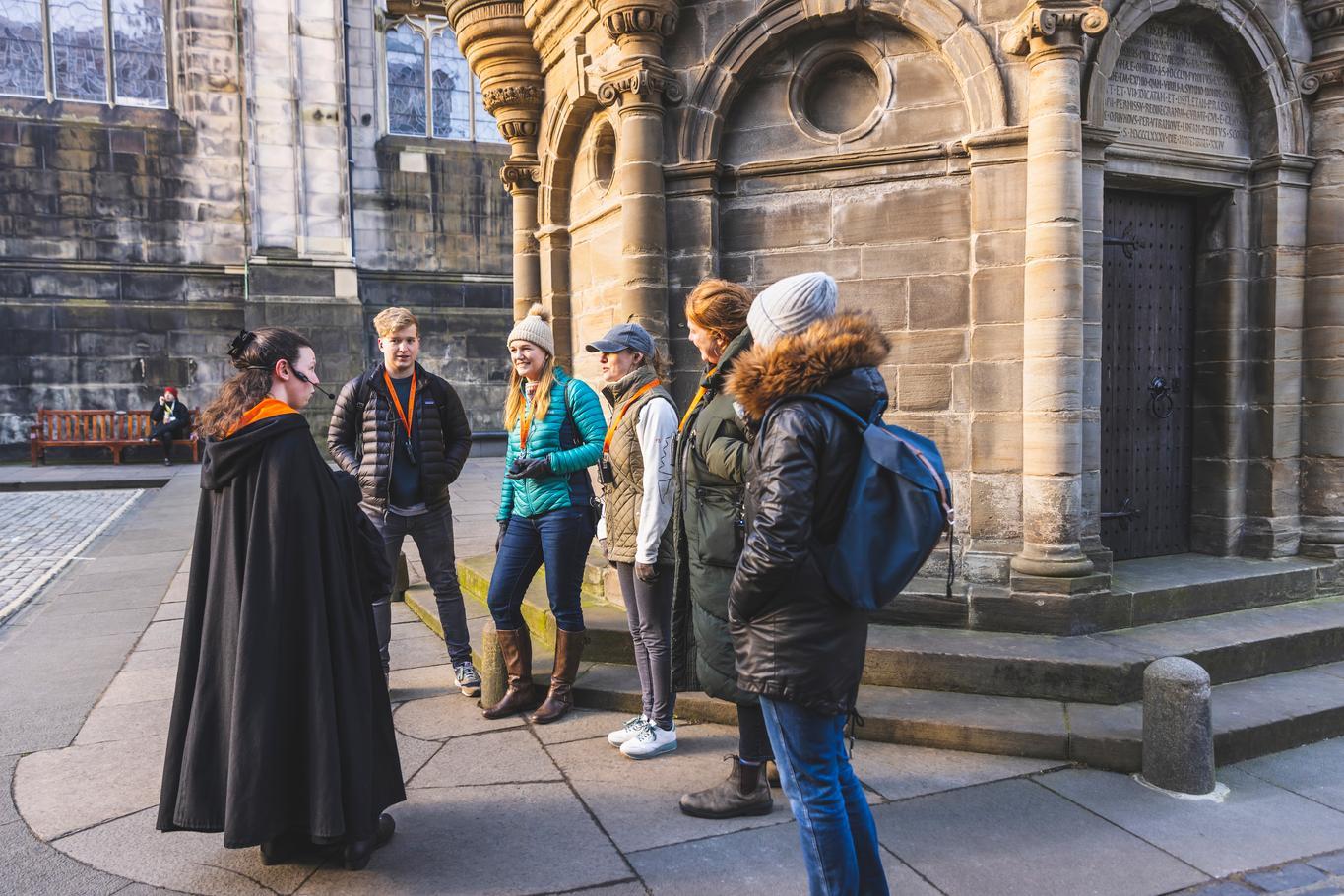 A group of people all standing around in a small group outside listening to a tour guide
